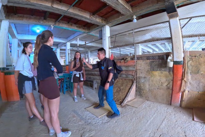 A group of people in an indoor setting with a concrete floor, metal fencing, and a partially visible roof structure. 3
