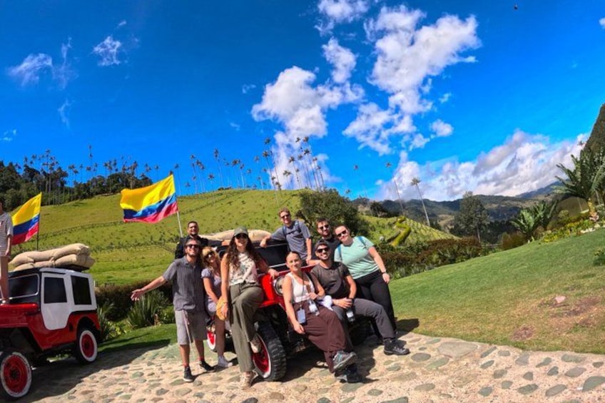 A group of people posing with a vehicle and flags on a grassy hill with a clear sky. 2