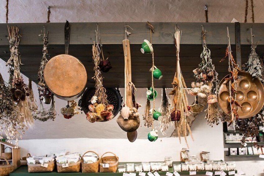 Various dried plants and natural elements hanging from a wooden beam, with baskets and containers on the floor. 2