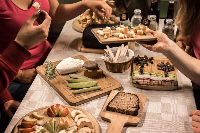 A group of people at a table with various food items including cheese, bread, and pickles. 1