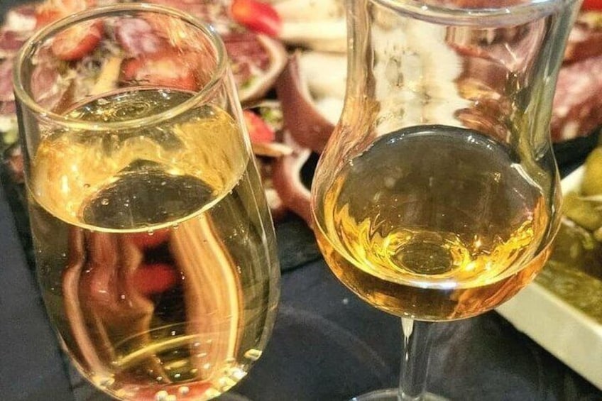 Two glasses of a golden liquid, likely wine, with a blurred background of food. 5