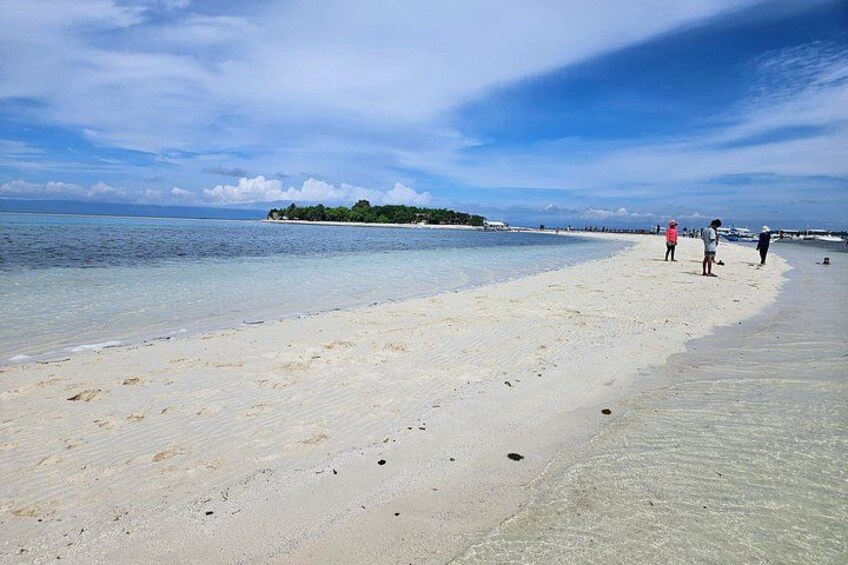 A beach with clear water, a distant island, and a few people walking. 3