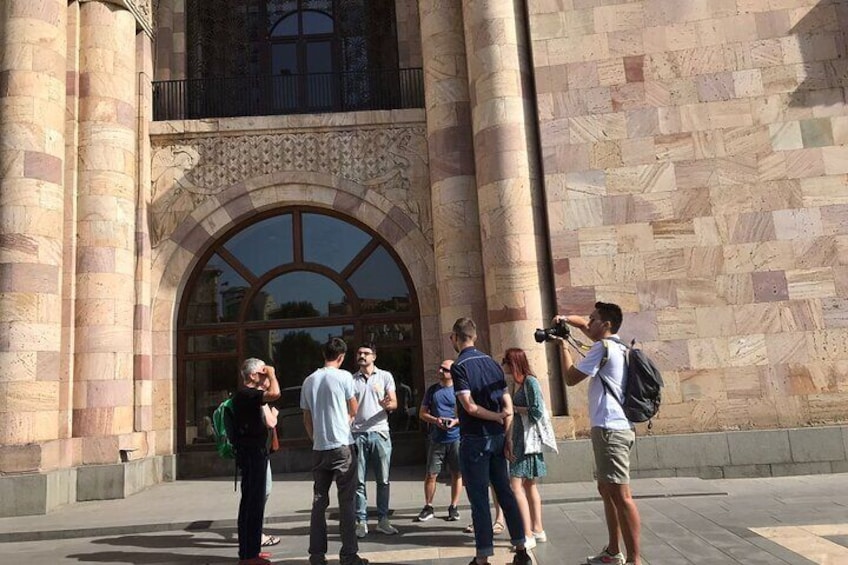 A group of people standing in front of a large stone building with an arched entrance. 2