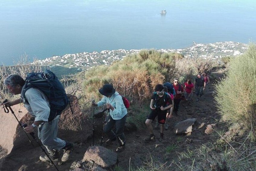 A group of hikers on a rocky trail with a coastal town in the background. 3