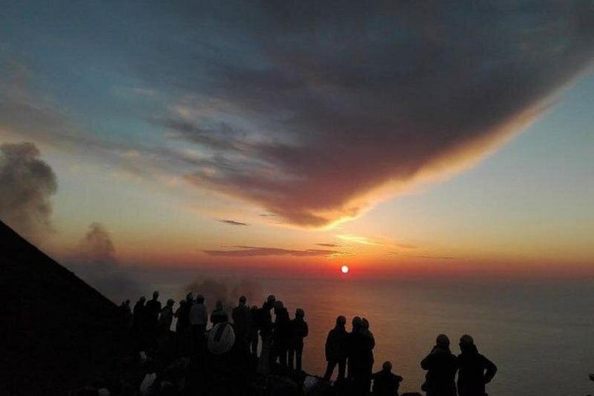 A sunset over a body of water with silhouettes of people watching. 1