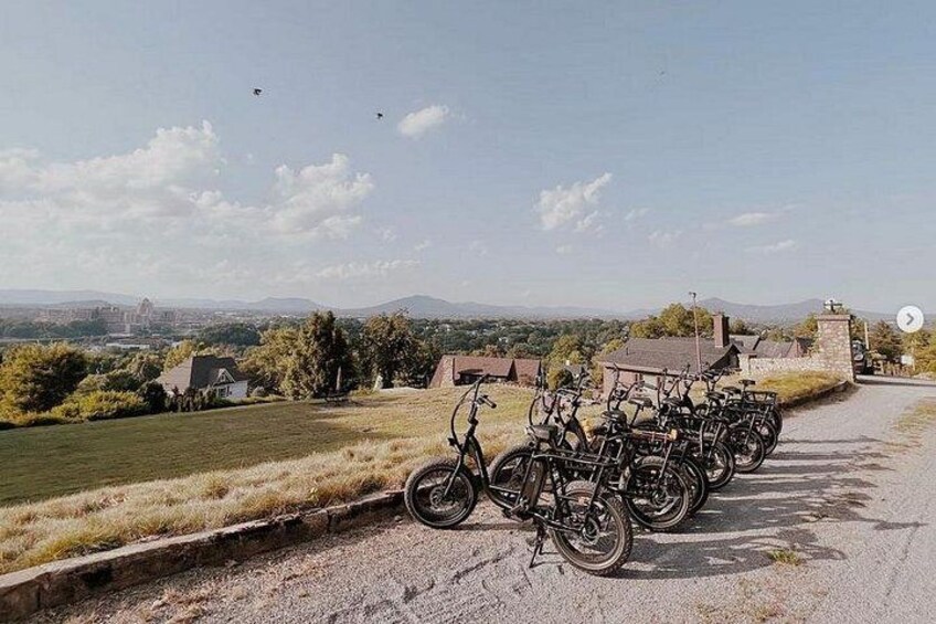 A gravel path with bicycles parked on the side, a stone wall, and a view of distant buildings and hills. 5
