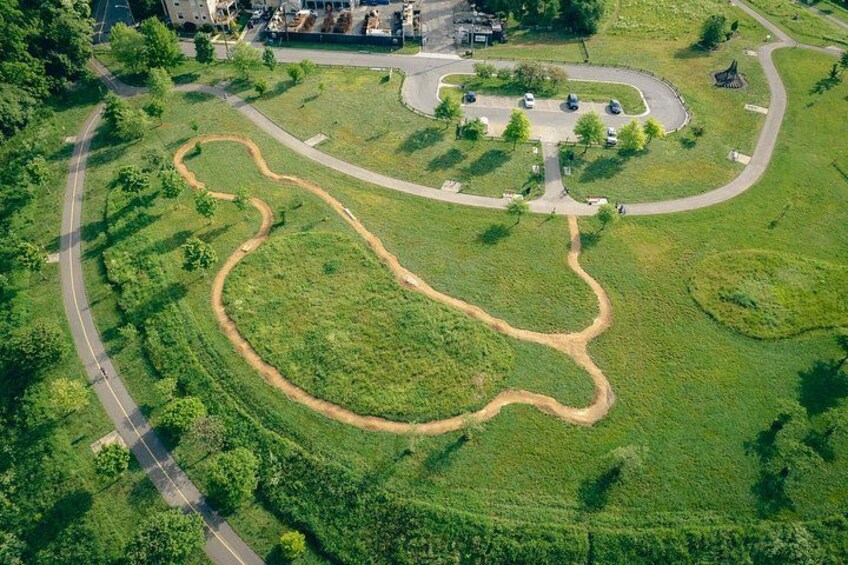 An aerial view of a park with winding paths, a central circular area, and surrounding greenery. 4