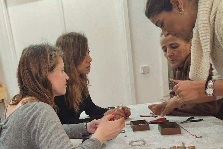 Trois personnes participent à une activité manuelle, peut-être la fabrication de bijoux, et disposent d’outils et de matériaux sur une table. 4