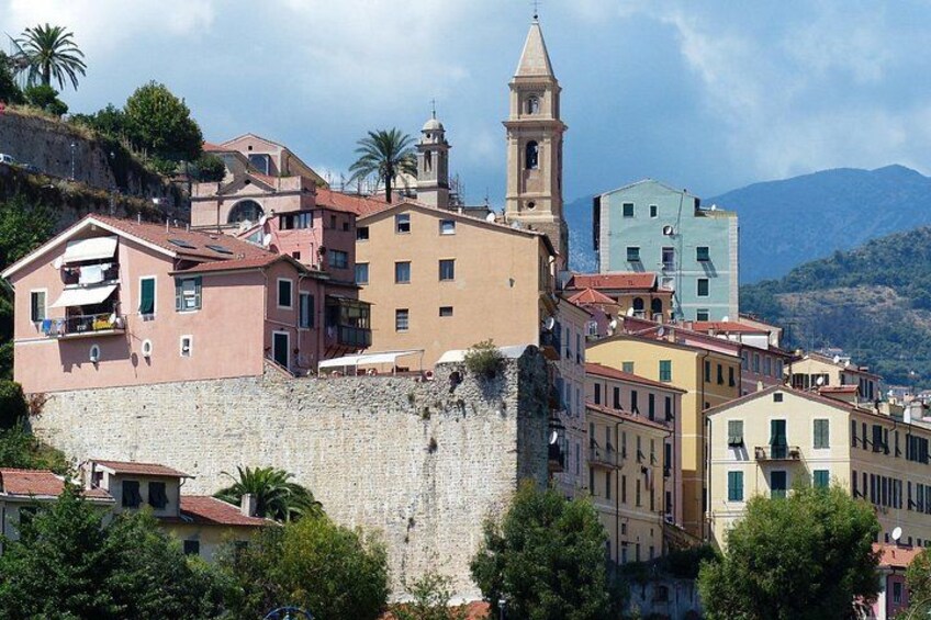A coastal town with colorful buildings, a prominent church tower, and a stone wall. 3