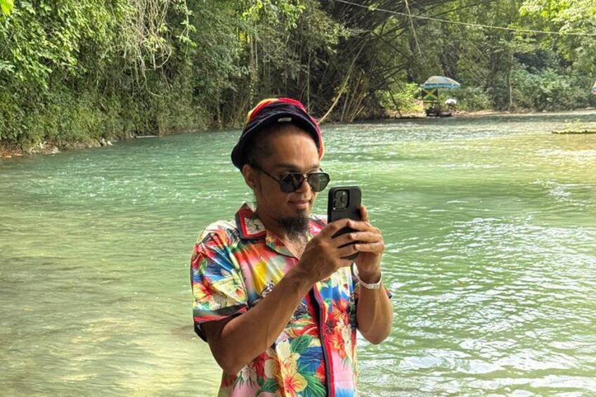 A person taking a photo by a river surrounded by greenery. 2