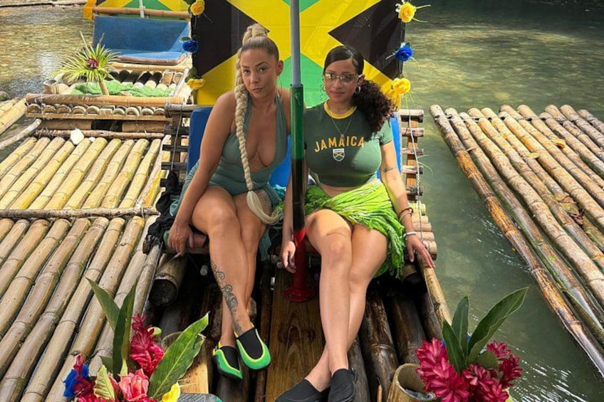 Two people on a floating platform with a 'Jamaica' t-shirt, surrounded by water and bamboo structures. 1