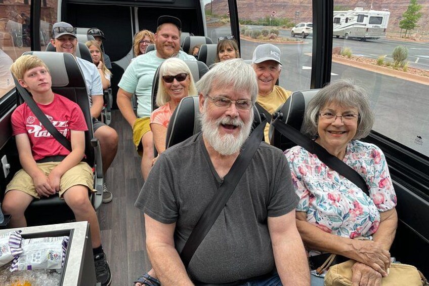 A group of people seated in a bus, with a mountainous landscape visible through the windows. 4