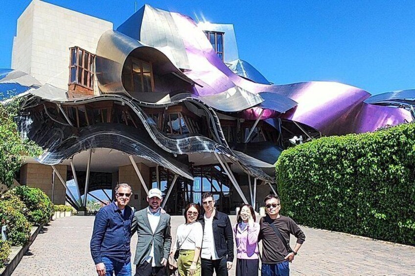 A group of people in front of a modern building with a unique, wavy roof design. 1