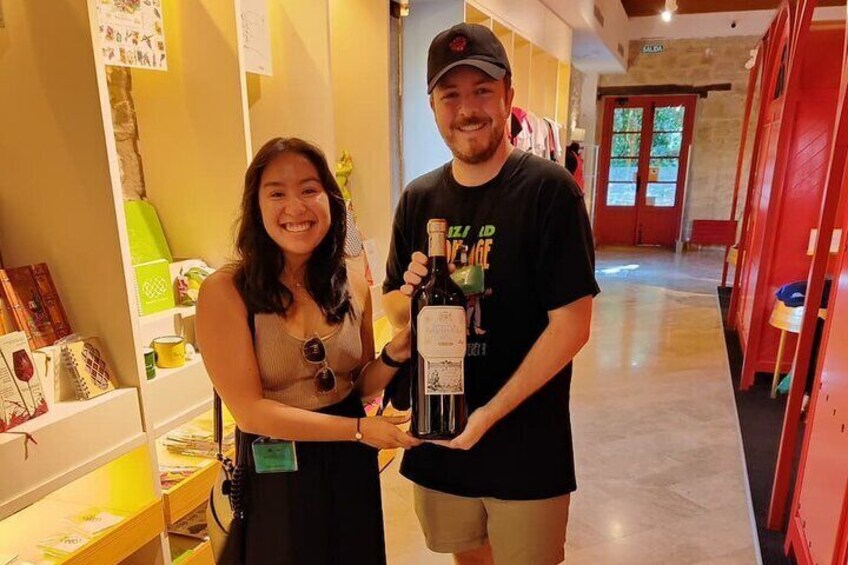 Two people holding a bottle of wine in a store with shelves of books and decorative items. 4