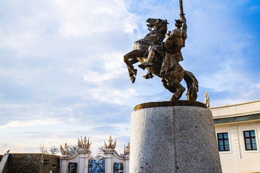 Una estatua de un jinete, un pedestal de piedra y un edificio con balcón al fondo. 5