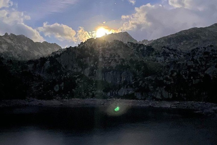 A mountain landscape with a lake in the foreground and the sun setting behind the mountains. 5