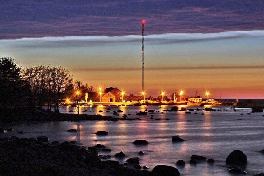 Een kustlandschap in de schemering met verlichte gebouwen, een vuurtoren en boten op het water. 2