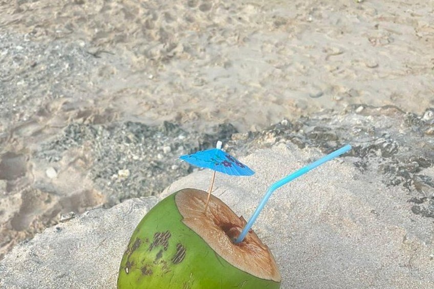 Un coco con una sombrilla azul y una pajita sobre arena. 2