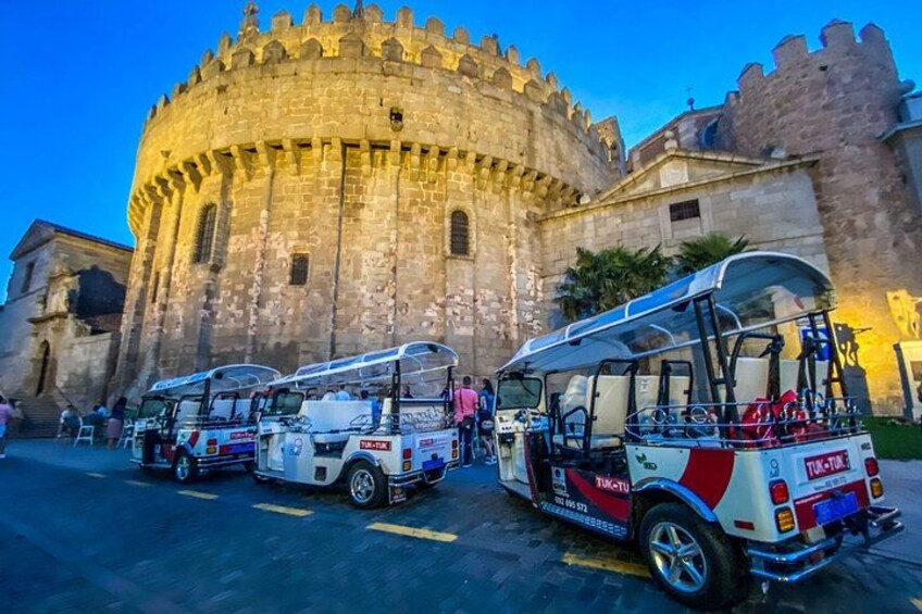 A historic stone building with a round tower, parked tour buses, and a clear sky. 1