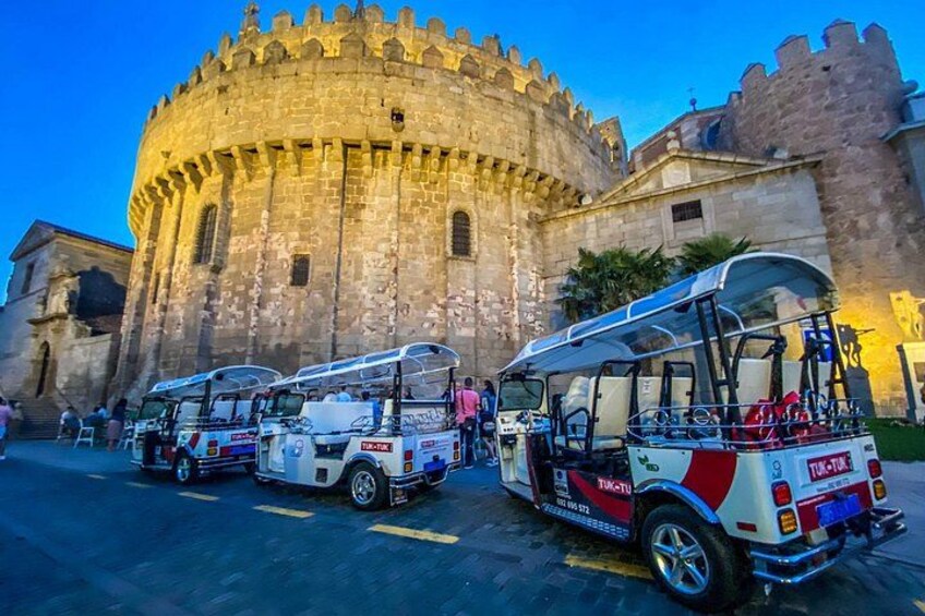 A historic stone building with a round tower, parked tour buses, and a clear sky. 1