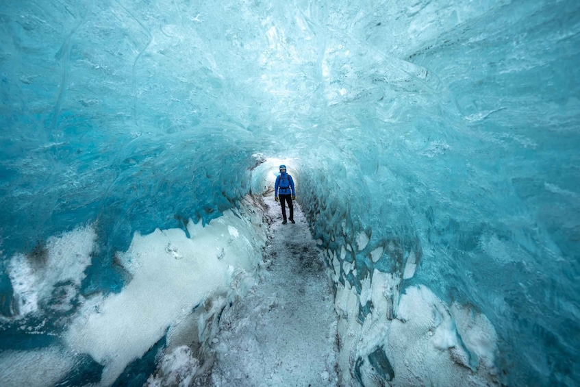 A person standing in a narrow, icy tunnel with walls of blue ice. 4