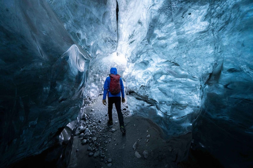A person in a blue jacket and red backpack walking through a narrow ice cave. 5