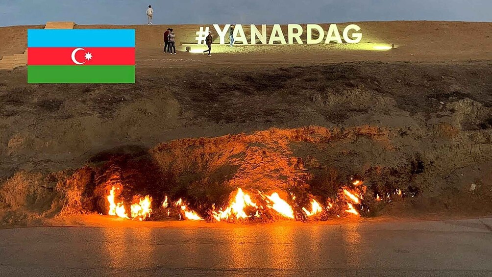 Ein großes Feuer brennt an einem Berghang, im Hintergrund weht eine Flagge und der Hashtag #YANARDAG ist zu sehen. 2