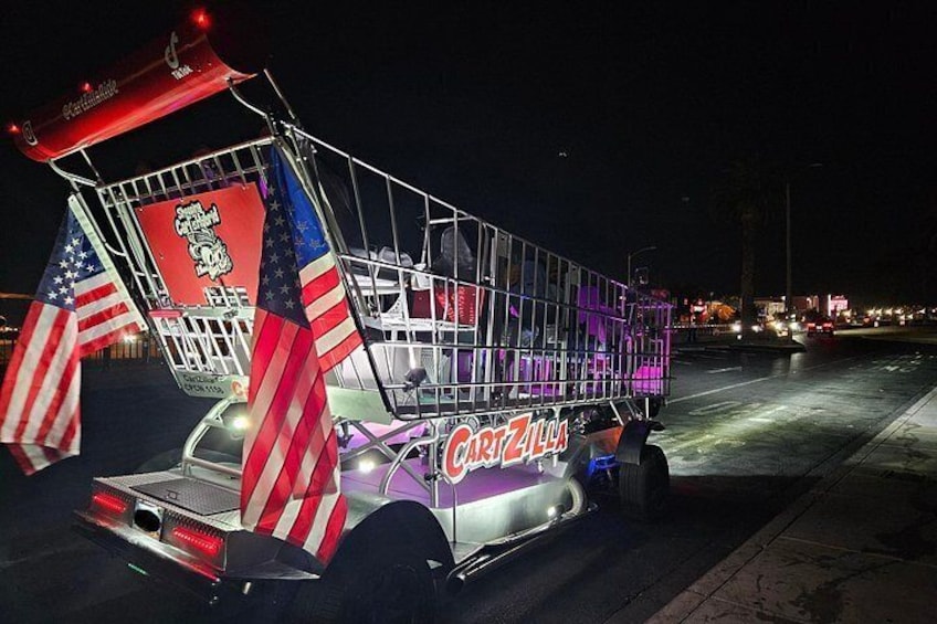 A brightly lit, decorated vehicle with 'Cartzilla' branding, American flags, and a red and white striped awning. 2