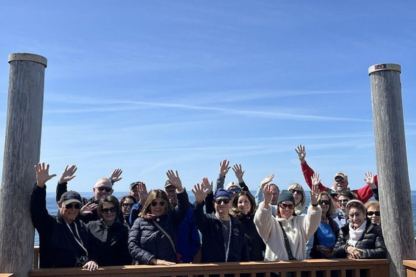 A group of people standing on a wooden deck with their hands raised, overlooking a body of water. 1
