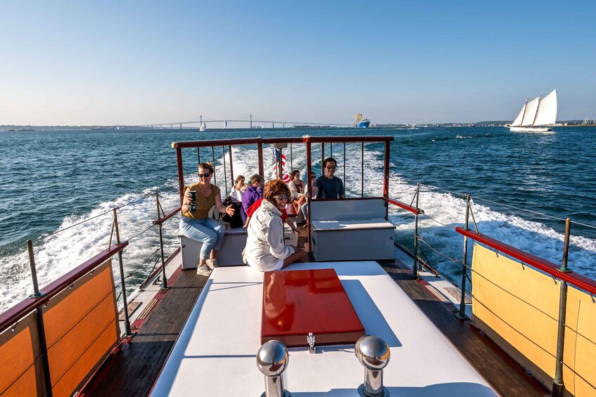 Ein Boot mit Passagieren genießt die Aussicht auf eine Brücke und Segelboote in der Ferne. 5