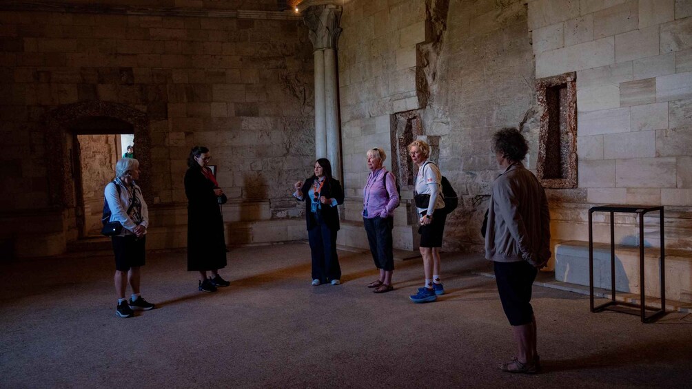 A group of people in a historical building with stone walls and columns. 4