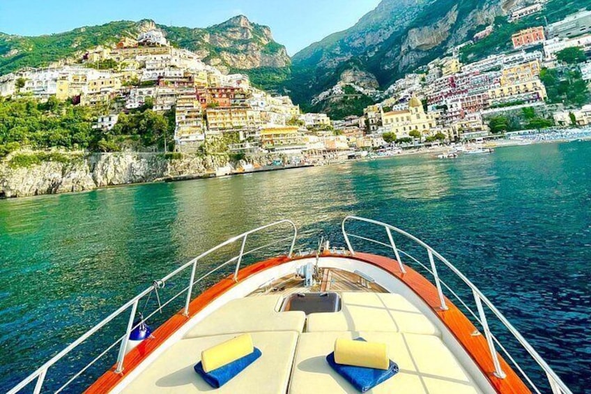 A boat with yellow cushions on the deck, a rocky coastline with colorful buildings, and a clear blue sea. 2