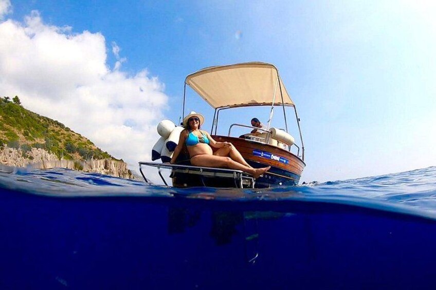 A boat with two people on it, one wearing a blue swimsuit, and a clear blue sky in the background. 5