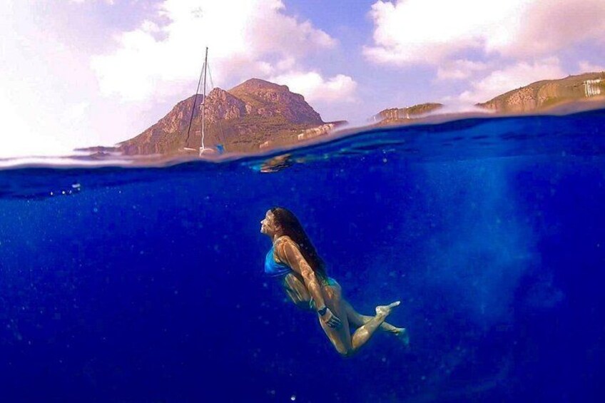 A mermaid swimming underwater with a sailboat and a mountain in the background. 4