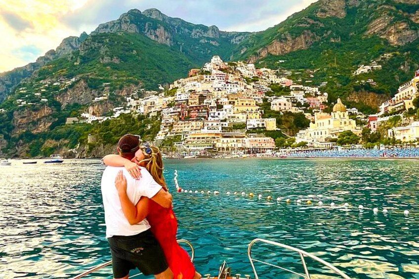 A couple embracing on a boat with a coastal town and mountains in the background. 1