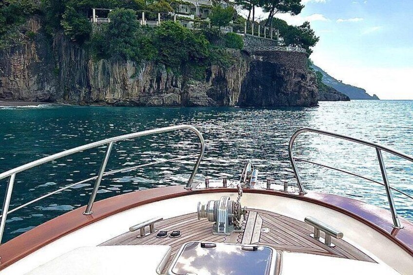 A boat's deck with metal railings, a wooden floor, and a view of a coastline with cliffs and greenery. 4