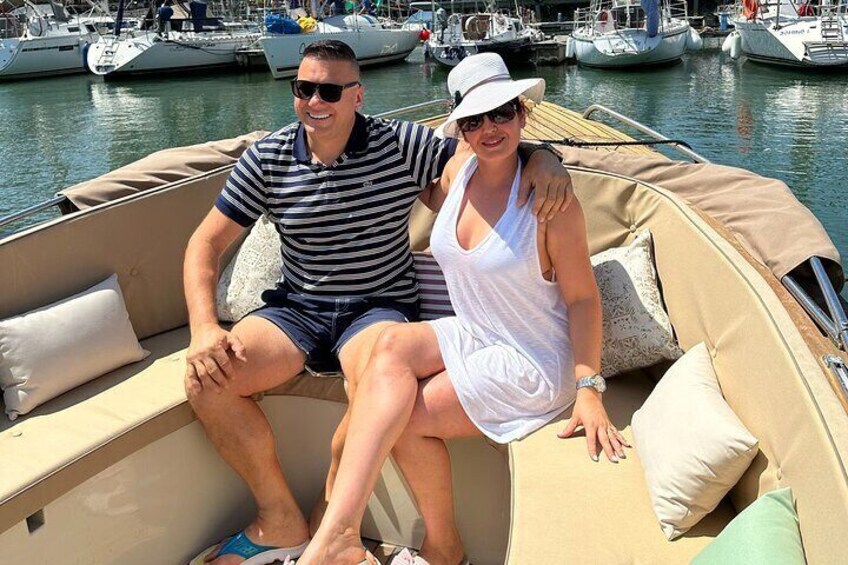Zwei Personen sitzen in einem Boot in einer Marina, im Hintergrund weitere Boote. 1