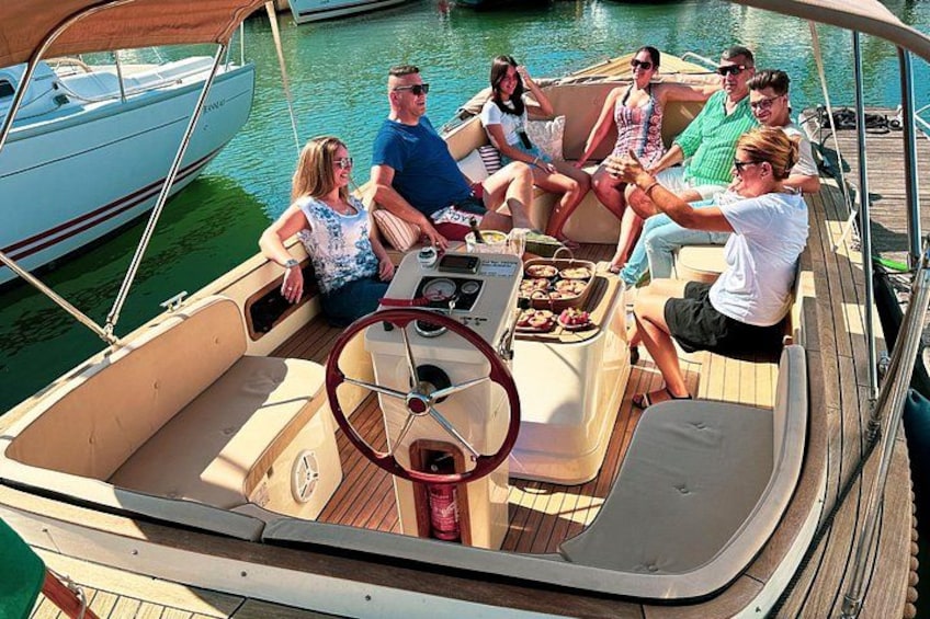 Un groupe de personnes se trouve sur un bateau équipé d’un volant, d’un pont en bois et d’une petite table où sont disposés des aliments. 4