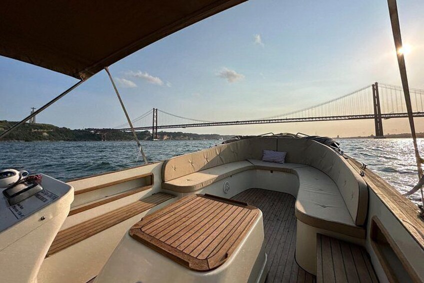 Cubierta de barco con piso de madera, asientos acolchados y una vista de un puente al fondo. 2