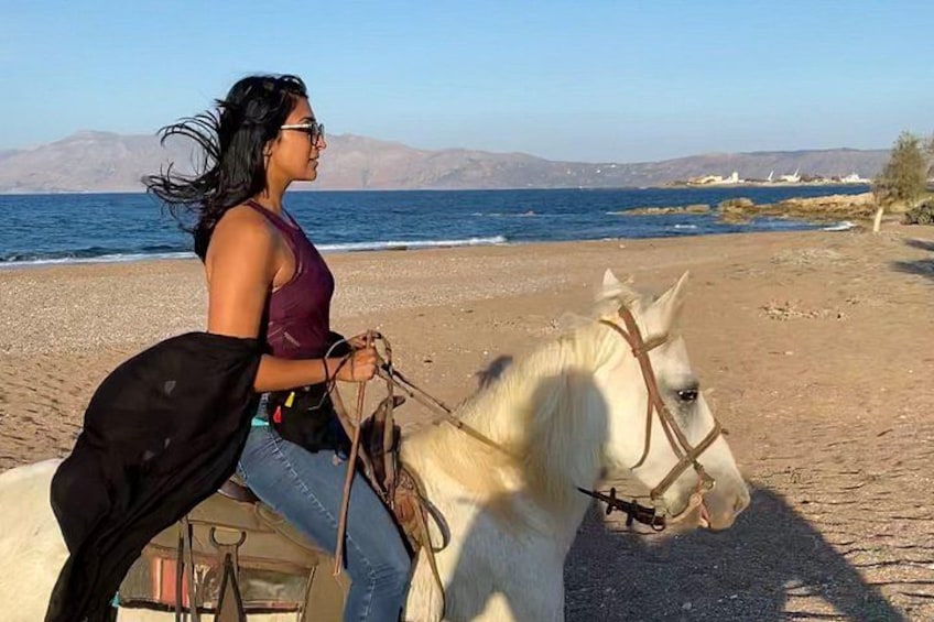 Una persona montando un caballo blanco en una playa, con montañas al fondo. 1