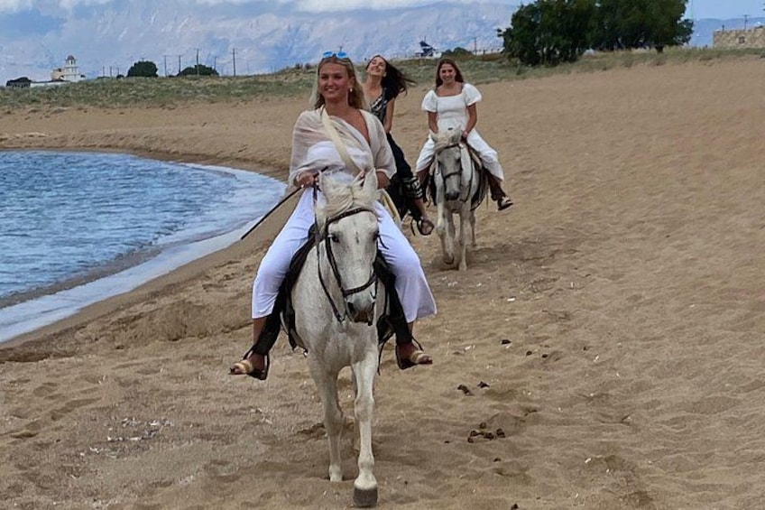 Tres personas montando a caballo a lo largo de una playa, con una masa de agua y un paisaje distante. 3