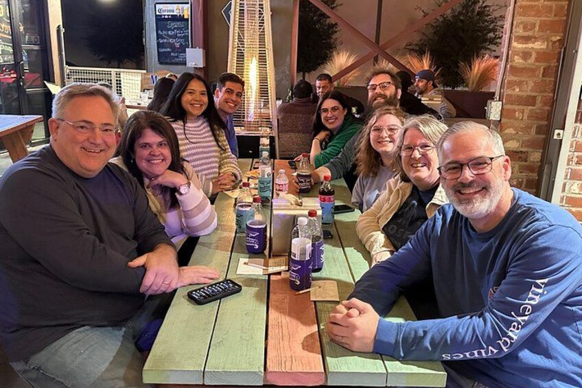 Un grupo de personas sentadas en una mesa de madera al aire libre, con bebidas y un menú a la vista. 5