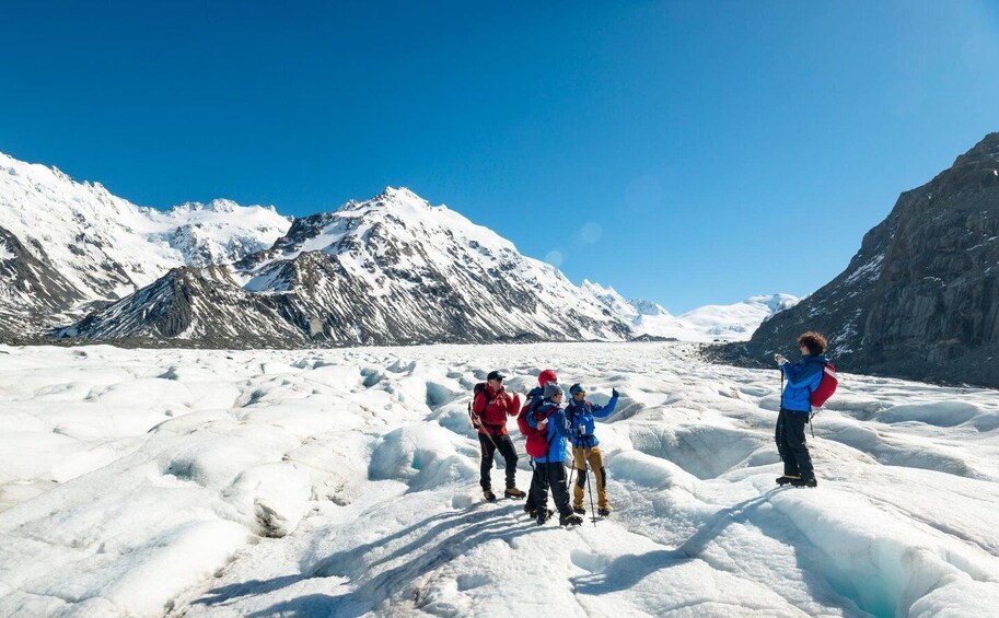 A group of people on a glacier with snow-covered mountains in the background. 1