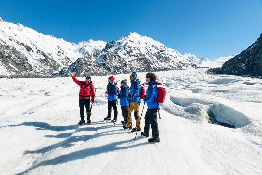 A group of people on a glacier with snow-covered mountains in the background. 3