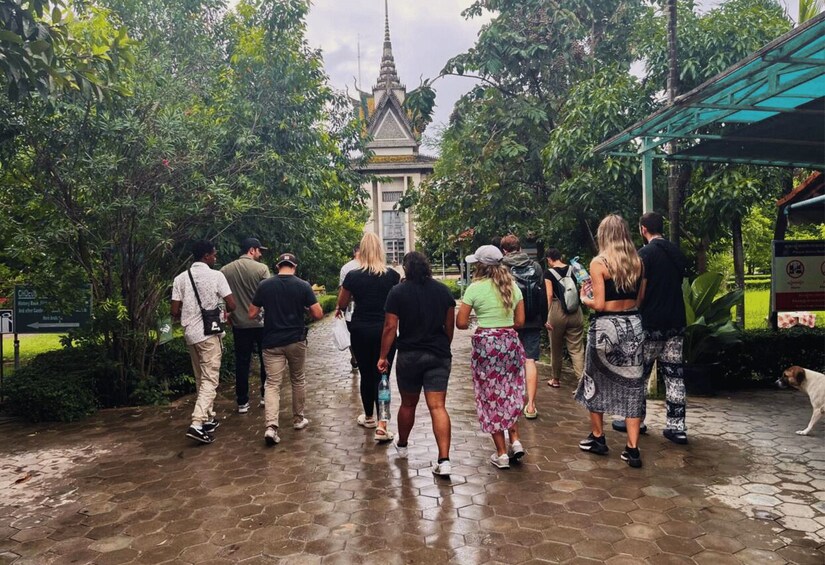 A group of people walking towards a temple with a traditional Thai roof, surrounded by lush greenery. 2