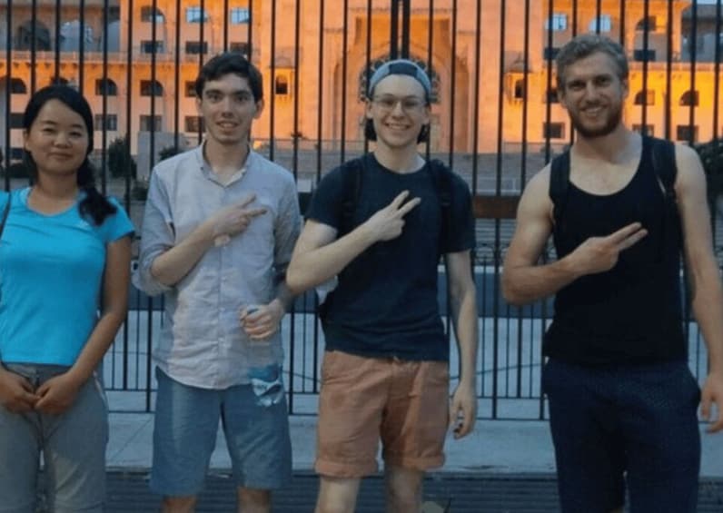 Quatre personnes se tiennent devant un bâtiment, derrière une clôture. 2