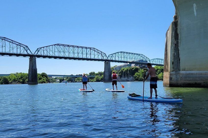 Tres personas haciendo paddleboard en un río debajo de un puente. 5