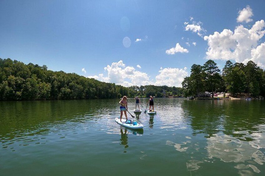 Tres personas haciendo paddleboard en un lago tranquilo rodeado de árboles. 2