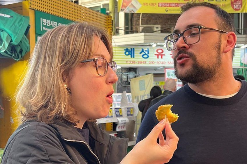 A person holding a piece of food, with a market stall in the background. 1