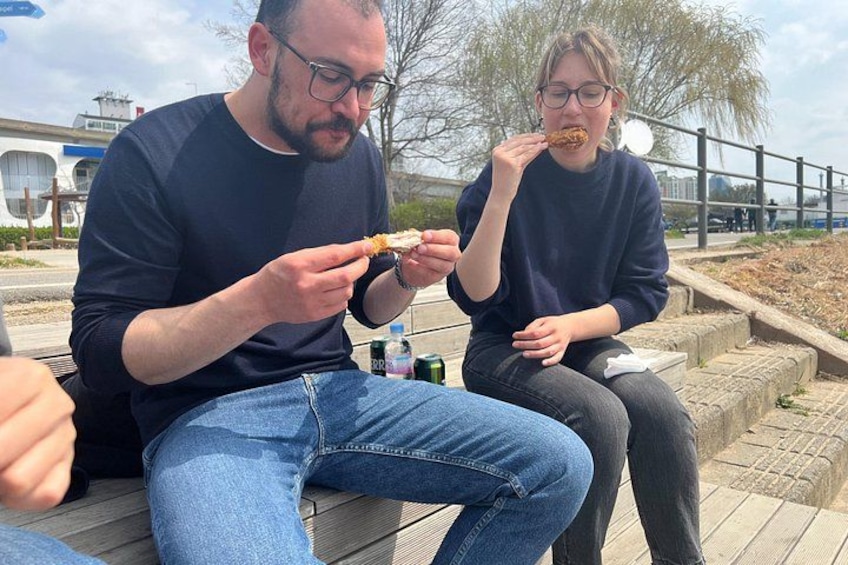Two people sitting on a wooden deck eating food. 5